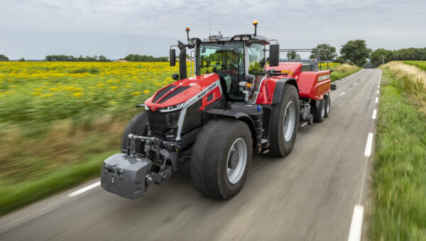 Massey Ferguson 9S tractor towing a baler down a country road next to a field of sunflowers