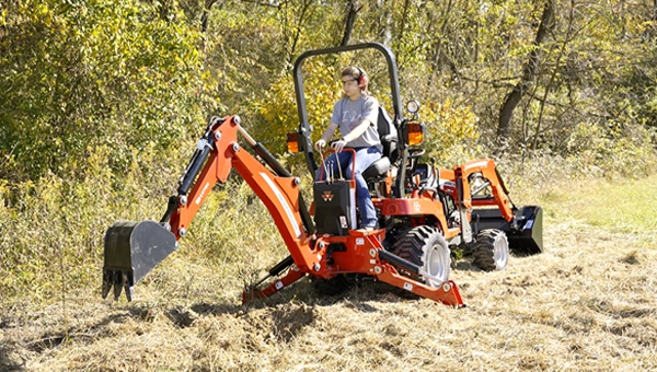 Massey Ferguson 1GC Series sub-compact tractor equipped with a backhoe attachment, ideal for digging and landscaping tasks in rugged terrain.