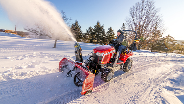 Massey Ferguson 1GC Series sub-compact tractor clearing snow with a powerful front-mounted snow blower attachment, perfect for winter maintenance.
