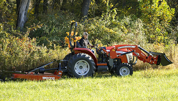 Massey Ferguson 2E Series compact tractor equipped with a front loader and rotary cutter, perfect for versatile field clearing and property maintenance.