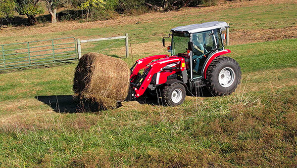 Massey Ferguson 2M Series compact tractor using a front-mounted bale spear, perfect for moving and stacking hay bales on farms and ranches.